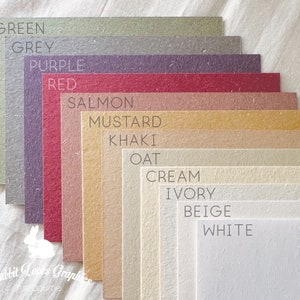 May include: A collection of 12 paper samples in various colors, including green, grey, purple, red, salmon, mustard, khaki, oat, cream, ivory, beige, and white. The paper samples are arranged in a fan shape, with the darkest color at the top and the lightest color at the bottom. The paper samples are all textured and have a natural look.