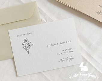 以下が含まれることがあります： クリーム色のウェディングステーショナリーセット。花のイラストと「SAVE THE DATE」の文字が入ったカード。Lilian & Gordanの名前、日付29/01/2022、場所が含まれています。封筒が見えます。