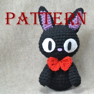 Könnte beinhalten: Eine handgefertigte schwarze Häkelkatze mit großen weißen Augen, lilafarbenen Ohren und einer roten Fliege. Das Wort "PATTERN" wird in roter Schrift über der Katze angezeigt. Bei diesem Artikel handelt es sich um ein Häkelmuster.