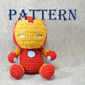 May include: A crocheted Iron Man toy with a red body, yellow face, and white eyes. The toy is sitting on a beige surface.