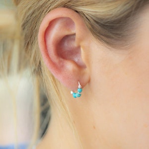 Può includere: Primo piano di un orecchio con un piccolo orecchino a cerchio d'argento con perline turchesi.