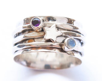 May include: A silver ring with multiple bands, featuring a small white star charm, a purple gemstone, and a light blue gemstone.
