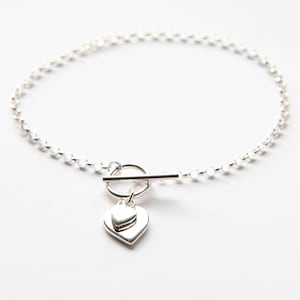 Op de afbeelding: Een zilveren armband met een toggle sluiting en een dubbele hart charme.