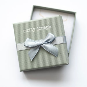 May include: A light green gift box with a light blue ribbon and bow. The box has the text "emily joseph" printed on the top.