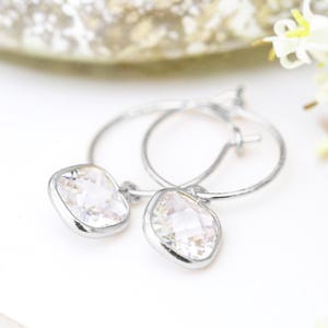 May include: Silver hoop earrings with a dangling square-shaped clear crystal.