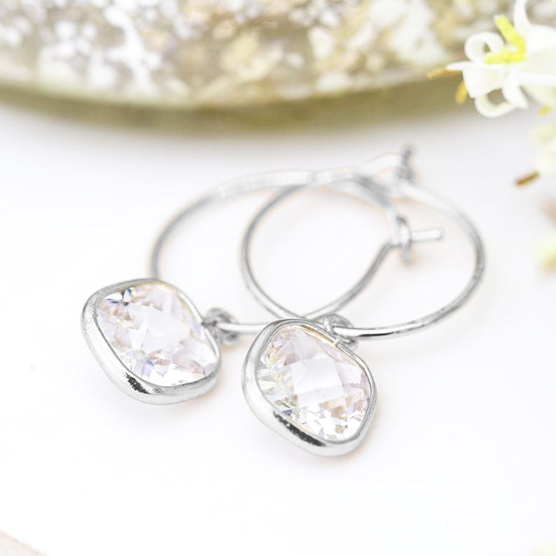 May include: Silver hoop earrings with a dangling square-shaped clear crystal.