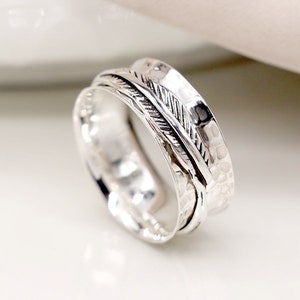 May include: A silver spinning ring with a hammered texture and a feather design. The ring is made of sterling silver and is a popular choice for meditation and mindfulness.
