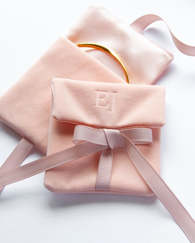 May include: A pink velvet jewellery pouch with a satin ribbon tied in a bow. The pouch is personalised with the initials "EJ".