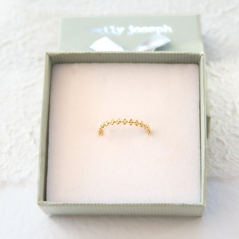May include: A delicate gold ring with a beaded design. The ring is displayed in a white box with the text "Shelly Joseph" on the lid.
