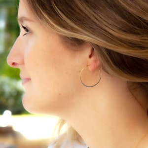 May include: A close-up of a woman's ear wearing a thin gold hoop earring.