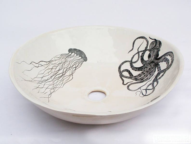 May include: Oval, off-white ceramic sink with a central drain hole. The sink features black illustrations of a jellyfish and an octopus. The jellyfish is on the left, and the octopus is on the right.