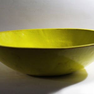 May include: A large, bright yellow ceramic bowl. The bowl has a smooth, glossy finish and a slightly rounded shape.