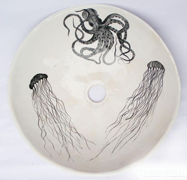 May include: A round, off-white ceramic sink basin featuring a hand-drawn octopus and two jellyfish in black ink. The octopus is at the top, and the jellyfish are on either side of the drain hole.