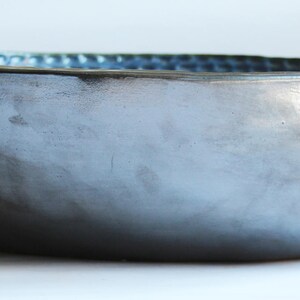 May include: A large, oval-shaped ceramic bowl with a dark gray exterior and a light blue interior. The bowl has a textured surface and a slightly uneven rim.