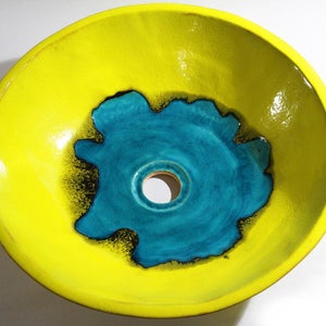 May include: A yellow ceramic sink with a turquoise blue center and a black rim. The sink has a round shape and a smooth, glossy finish.