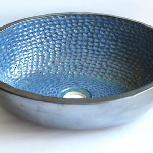 May include: A blue ceramic sink with a textured surface. The sink is round and has a small drain hole in the center.