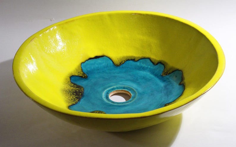 May include: A yellow ceramic sink with a turquoise blue center and a drain hole. The sink has a unique, organic shape.