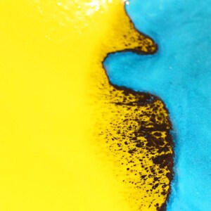 May include: Close-up of a ceramic plate with a yellow and blue glaze. The glaze is separated by a black line, creating a unique design.