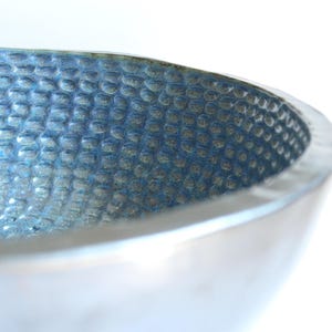May include: A close-up of a blue ceramic bowl with a textured surface. The bowl is slightly curved and has a white rim.