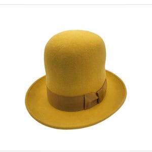 May include: Mustard yellow top hat with a brown ribbon band and bow. The hat has a rounded crown and a wide brim. A classic accessory for costumes or special events.