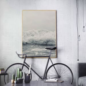 May include: A black bicycle with a wooden frame and a white wall in the background. A framed photograph of ocean waves hangs on the wall.