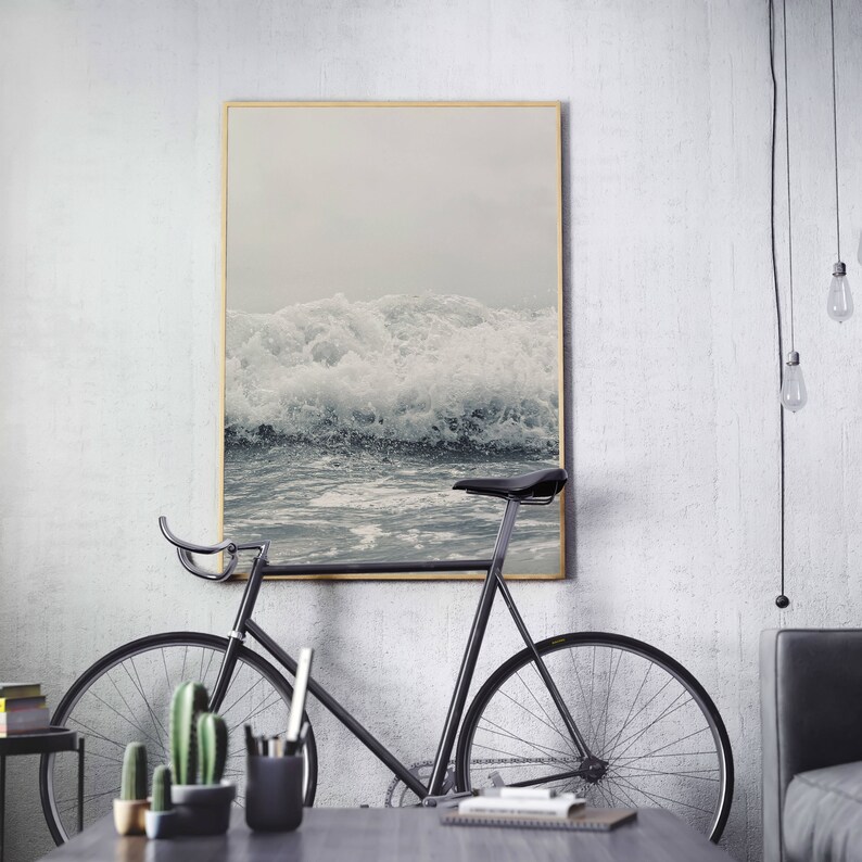 May include: A black bicycle with a wooden frame and a white wall in the background. A framed photograph of ocean waves hangs on the wall.