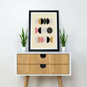 May include: A framed print with a geometric design of overlapping circles in black, gold, pink, and light gray on a cream background.