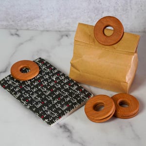 Puede incluir: Tres anillos de madera con un agujero en el centro. Los anillos están apilados uno encima del otro. Los anillos son de color marrón claro.