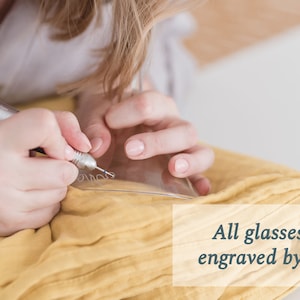 May include: A person is hand-engraving a glass with a small tool. The text "All glasses are engraved by hand" is visible in the image.