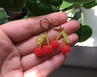 May include: A pair of beaded cherry earrings with gold hooks. The cherries are red and the stems are green.