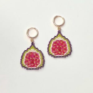May include: A pair of gold hoop earrings with a beaded fig design. The fig is a cross-section of a purple, pink, and white fig with a green outer layer.