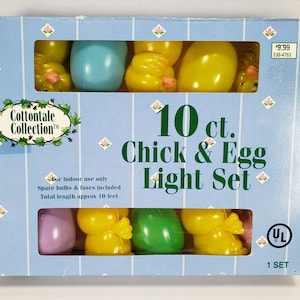 May include: A box of 10 count Chick & Egg Light Set from the Cottontale Collection. The set features yellow chicks and pastel colored eggs. The box is blue with a white and pink floral pattern. The lights are for indoor use only and come with spare bulbs and fuses. The total length of the lights is approximately 10 feet. The box also includes a UL safety certification label.