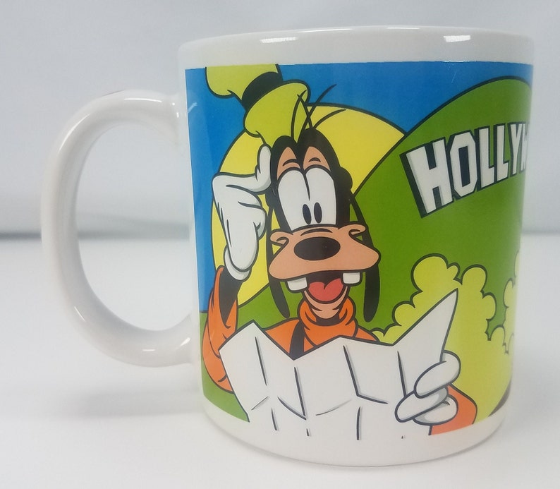 Puede incluir: Taza de cer&aacute;mica blanca con una imagen de dibujos animados de Goofy mirando un mapa con el texto "HOLLYWOOD" en el lateral.
