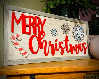 May include: A white wooden sign with the words "Merry Christmas" in red letters. The sign is decorated with blue and white snowflakes and a red and white candy cane.