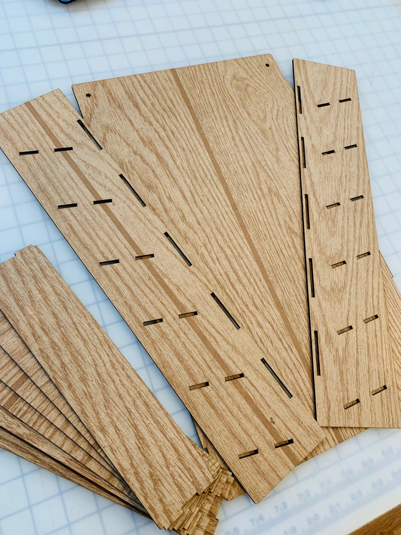 May include: A set of wooden craft pieces with slots cut out. The pieces are various sizes and shapes, and have a wood grain pattern.