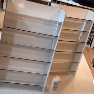 May include: Two white cardboard shelves with five shelves each. The shelves are empty and have a black border around each shelf. A bottle of glue is in the foreground.