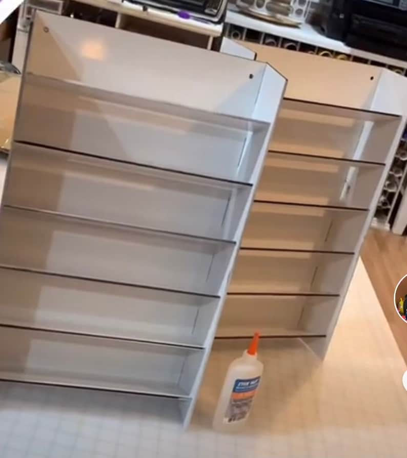 May include: Two white cardboard shelves with five shelves each. The shelves are empty and have a black border around each shelf. A bottle of glue is in the foreground.