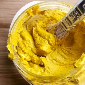 May include: A glass jar filled with a thick, yellow, creamy substance. A paintbrush is partially submerged in the jar.