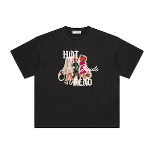May include: A black short-sleeve t-shirt featuring a graphic print of three figures dressed in Halloween costumes, including a ghost, a skeleton, and a pumpkin-headed character. The text "HOT GHOULS READ" is printed in white lettering.
