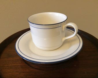 May include: A white teacup and saucer with a blue trim. The saucer has a blue band around the edge.