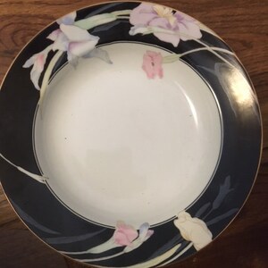 May include: A white soup bowl with a black rim and floral design. The flowers are pink, purple, and yellow. The bowl has a gold trim.