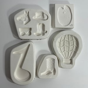 May include: Set of seven white silicone molds for making various shapes, including a cowboy boot, a hot air balloon, a musical note, a wagon, a cowboy hat, a horse, and a paint palette.