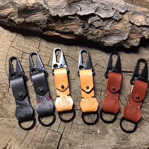 May include: Six leather keychains with metal clips and rings. The keychains are in different colors, including black, brown, and tan.
