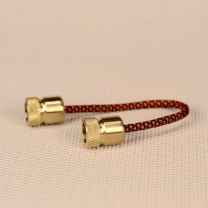 May include: A close-up of a fidget toy with two brass beads and a black and orange cord. The cord is woven with a diamond pattern.