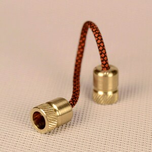May include: Two brass fidget toys with a black and orange cord connecting them. The toys are round with a grooved texture.