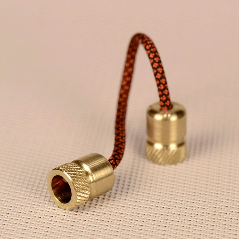 May include: Two brass fidget toys with a black and orange cord connecting them. The toys are round with a grooved texture.