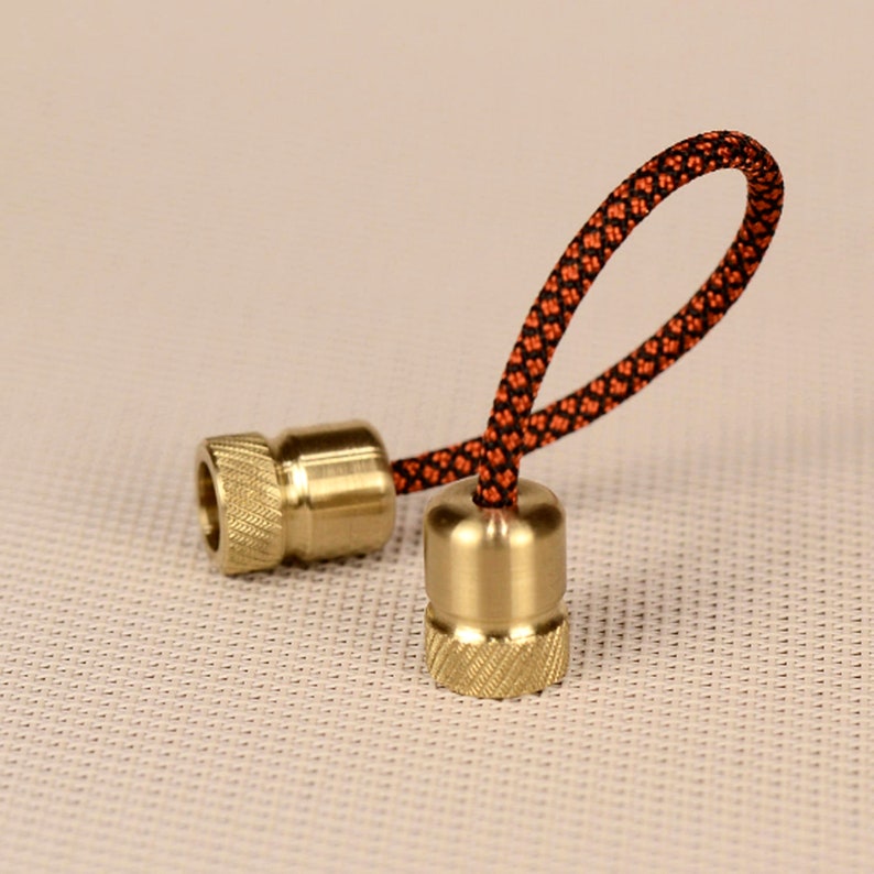 May include: Two brass beads with a black and orange cord threaded through them. The beads have a threaded design and are used for fidgeting or as a keychain.