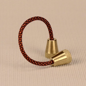 May include: A pair of brass fidget toys connected by a black and orange cord. The toys are shaped like cones with a textured surface.