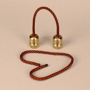 May include: A pair of brass fidget toys connected by a black and orange cord. The cord is looped into a heart shape.
