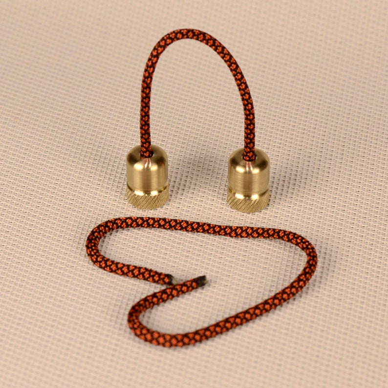 May include: A pair of brass fidget toys connected by a black and orange cord. The cord is looped into a heart shape.